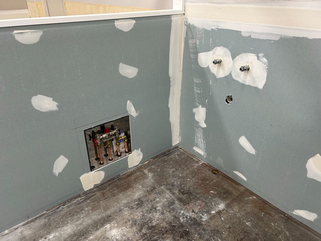 A wide shot of a room under renovation, showing moisture-resistant green drywall with plastered joints and patches.